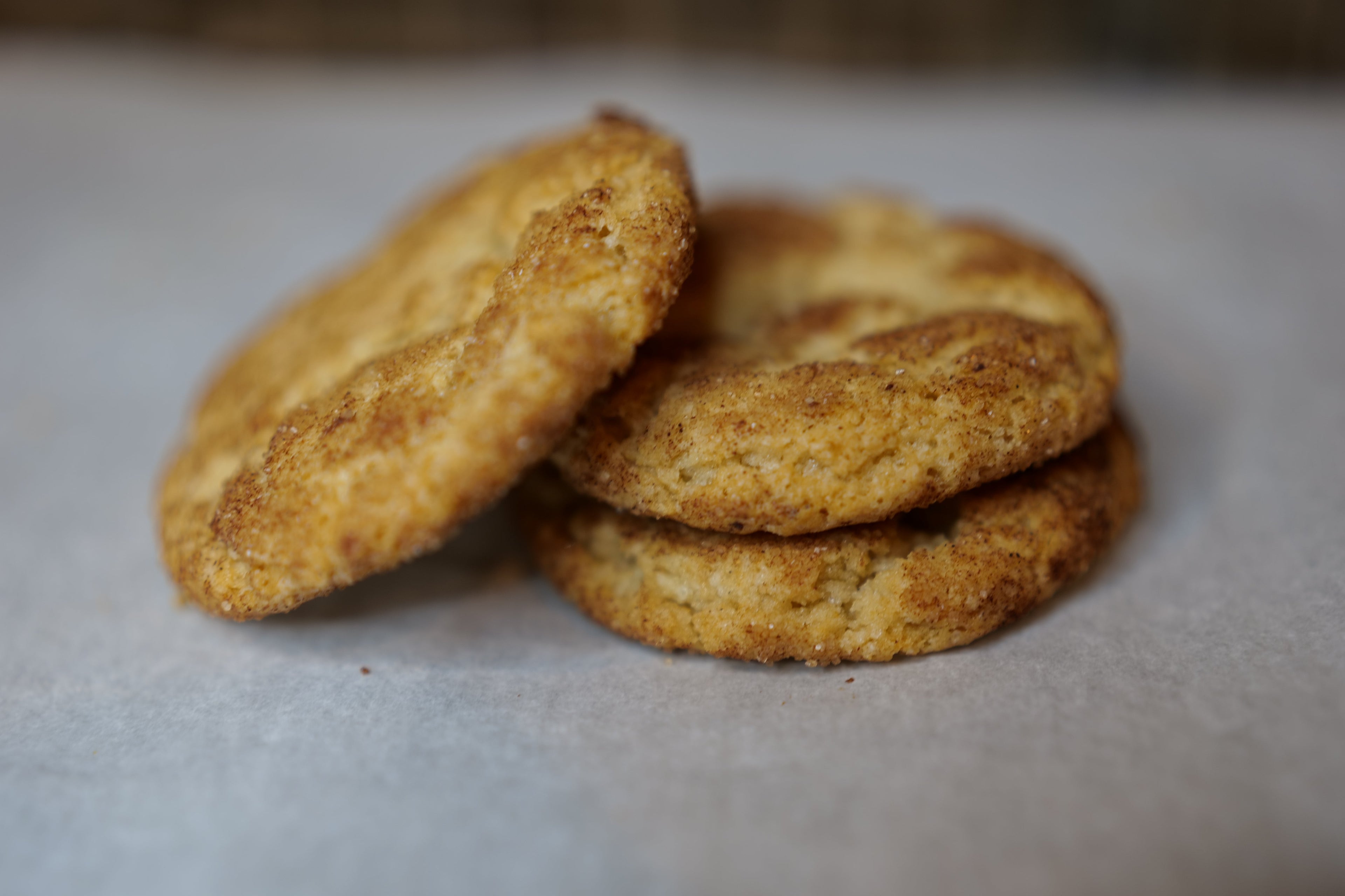 Three snickerdoodle cookies stacked on a light gray surface